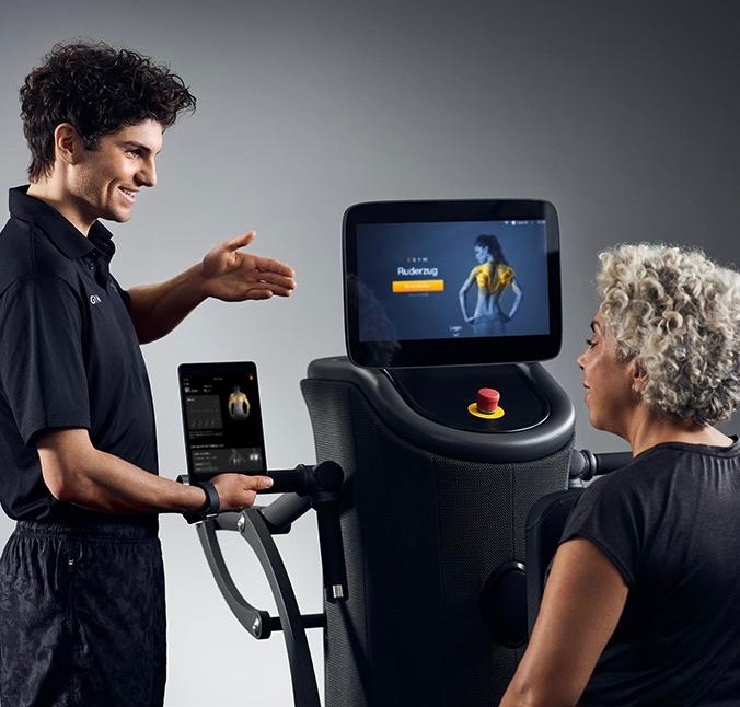 Coach hjälper medlem vid EGYM-maskin med personlig skärm