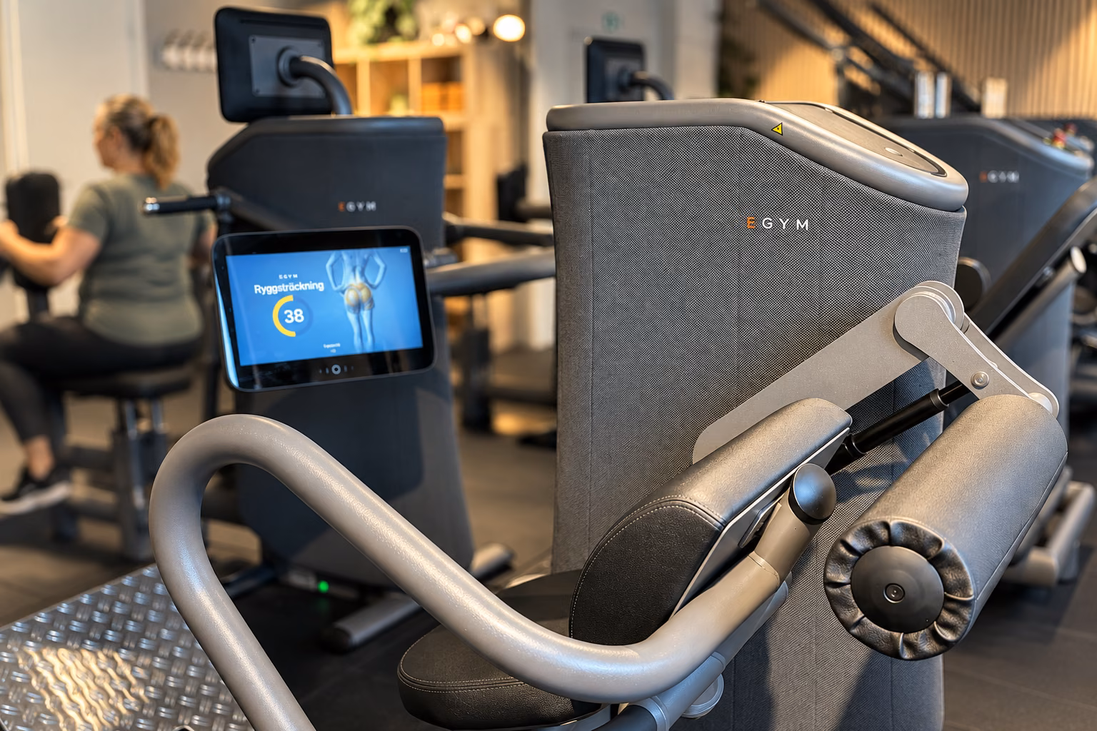 Närbild på en EGYM-maskin med träning i bakgrunden