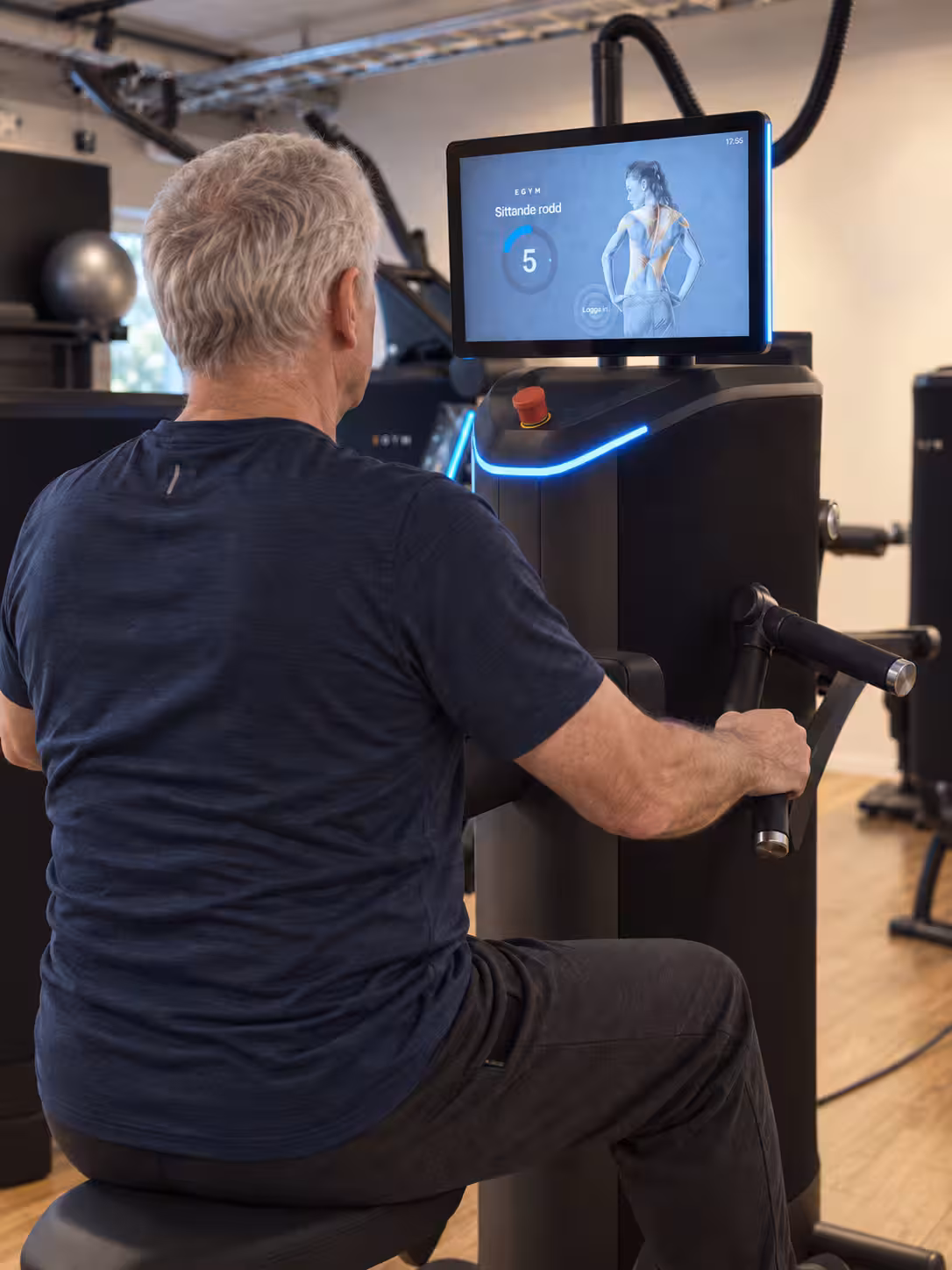 Äldre man sedd bakifrån vid en EGYM-maskin för sittande rodd