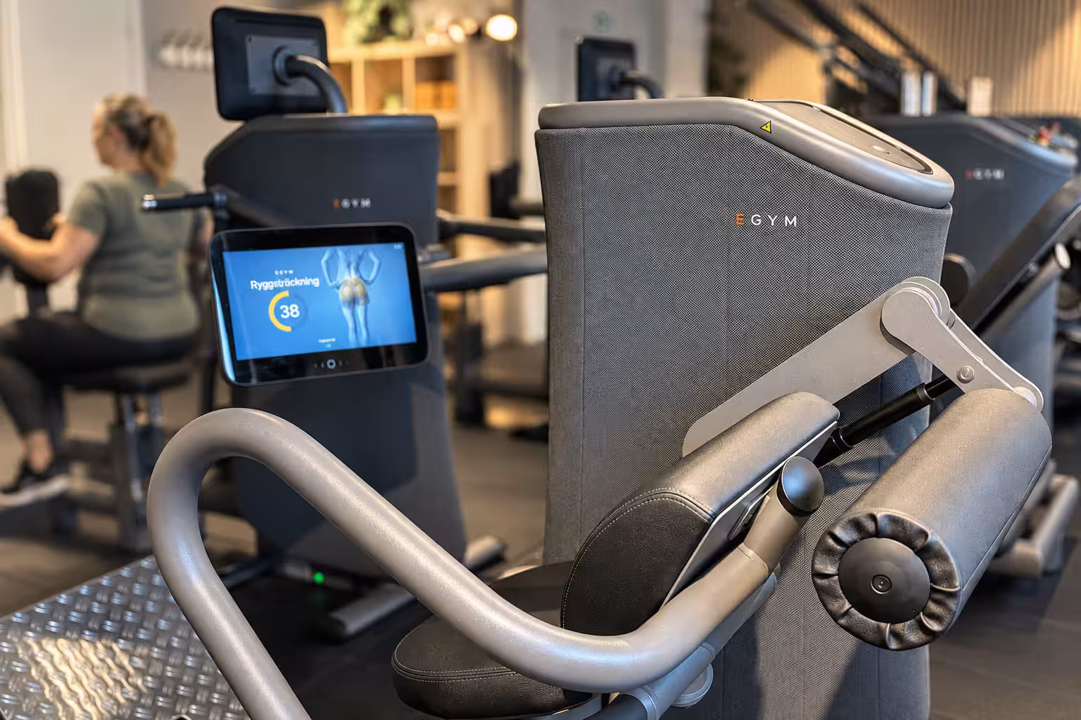 Närbild på en EGYM-maskin med träning i bakgrunden